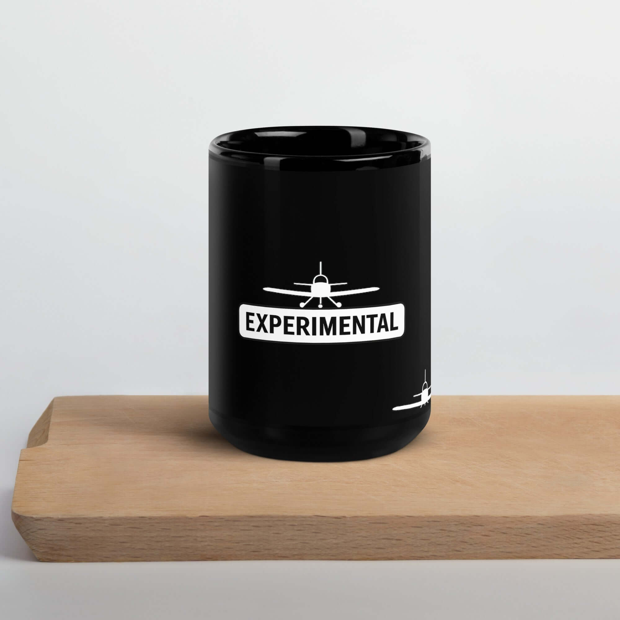 Black glossy ceramic mug with 'EXPERIMENTAL' text and airplane graphic on a wooden surface.